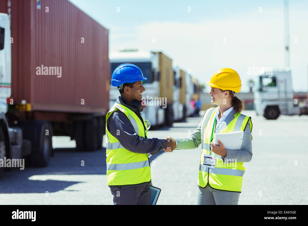 Arbeiter und Geschäftsfrau Händeschütteln in der Nähe von LKWs und Containern Stockfoto