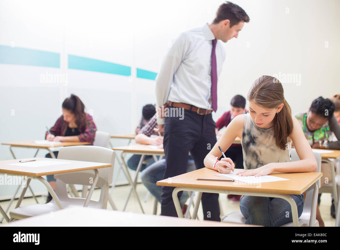 Männliche Lehrer, die Aufsicht über Schüler schreiben ihre GCSE Prüfung im Klassenzimmer Stockfoto