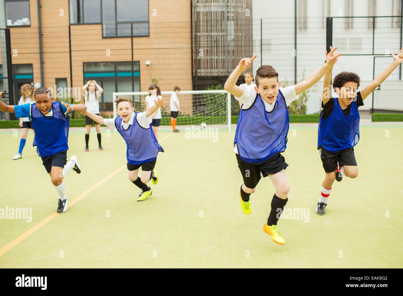 Schuljungen Sport Uniformen mit Fußballplatz vor Schule erhobenen Armen ausgeführt Stockfoto