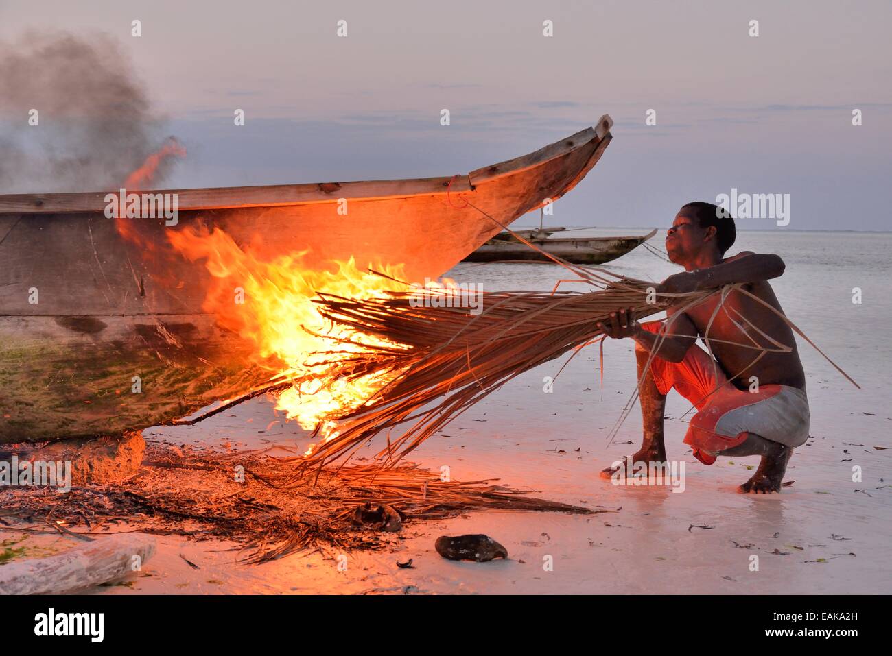 Fischer Rauchen sein Boot mit brennenden Palme Wedel, um die Oberfläche zu härten und Ungeziefer, Dongwe Strand, Dongwe, Zanzibar entfernen Stockfoto