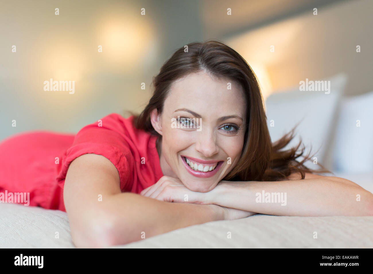 Portrait von lächelnden mittleren Erwachsenenalter Frau roten Kleid auf Bett im Schlafzimmer Stockfoto