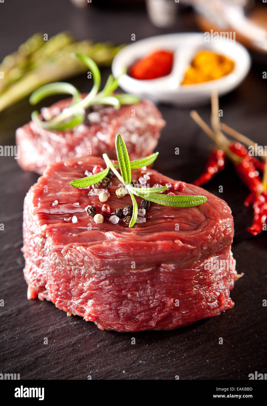 Stücke von roten rohes Fleisch Steaks mit Rosmarin auf schwarzen Steinoberfläche serviert. Stockfoto