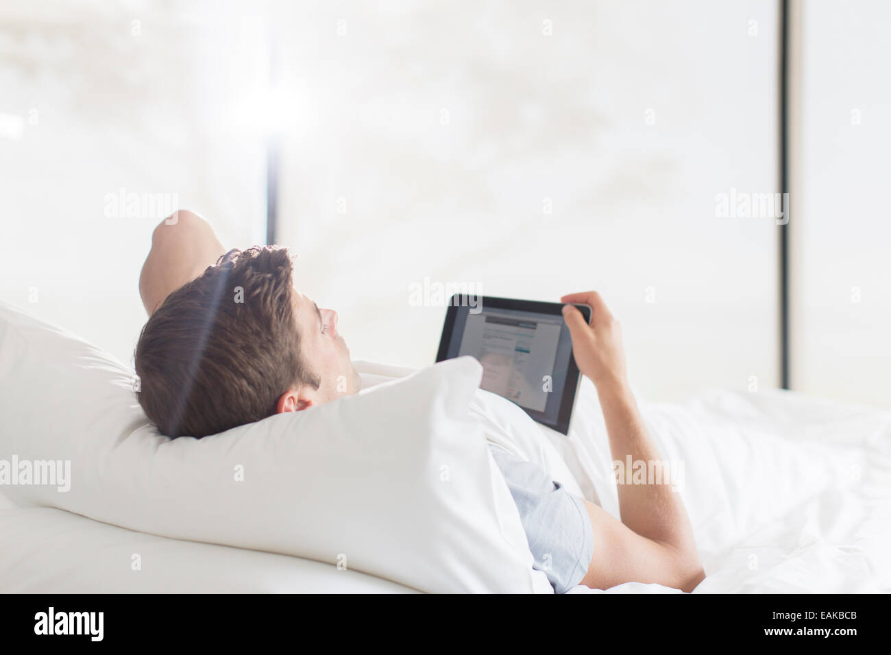 Junger Mann auf dem Bett liegend und mit tablet Stockfoto
