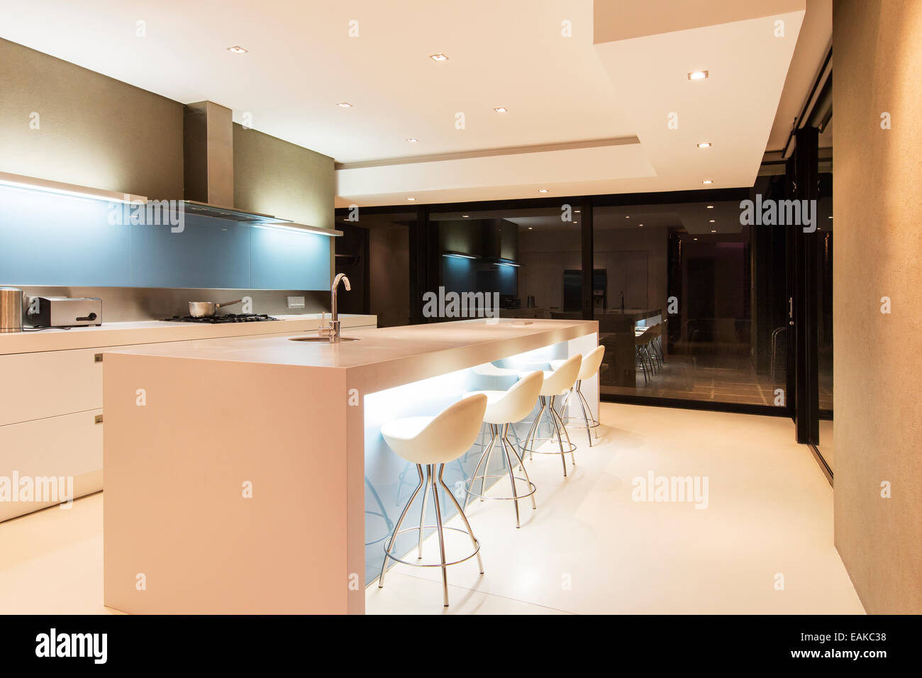 Moderne weiße Küche mit Kochinsel und Hocker, die nachts beleuchtet Stockfoto
