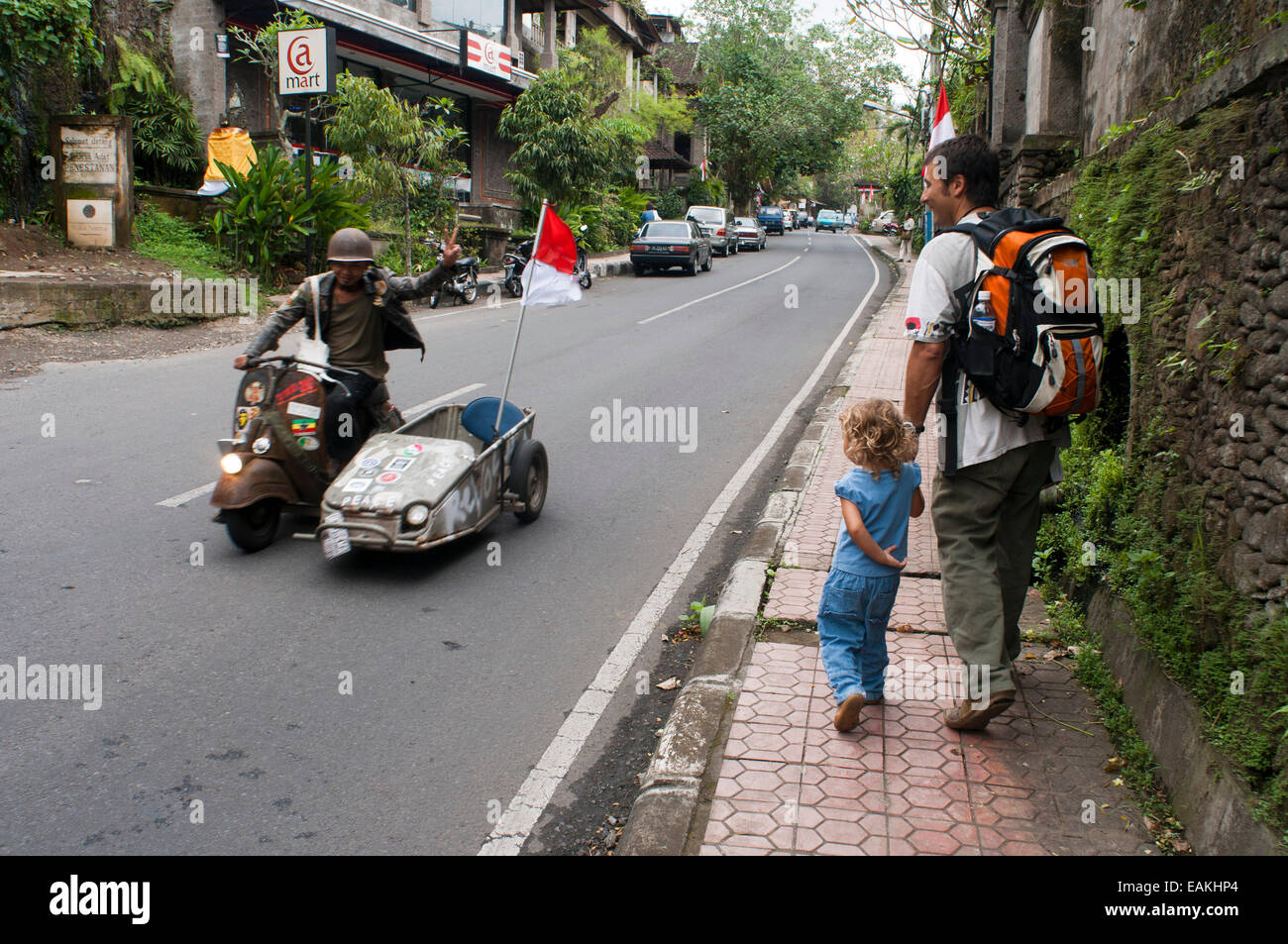 Ein Tourist mit einem Kind treffen ein Mann verkleidet als ein alter Soldat mit einem Beiwagen-Motorrad. Indonesien. Ubud.  Straßenszene Ubud Bali In Stockfoto