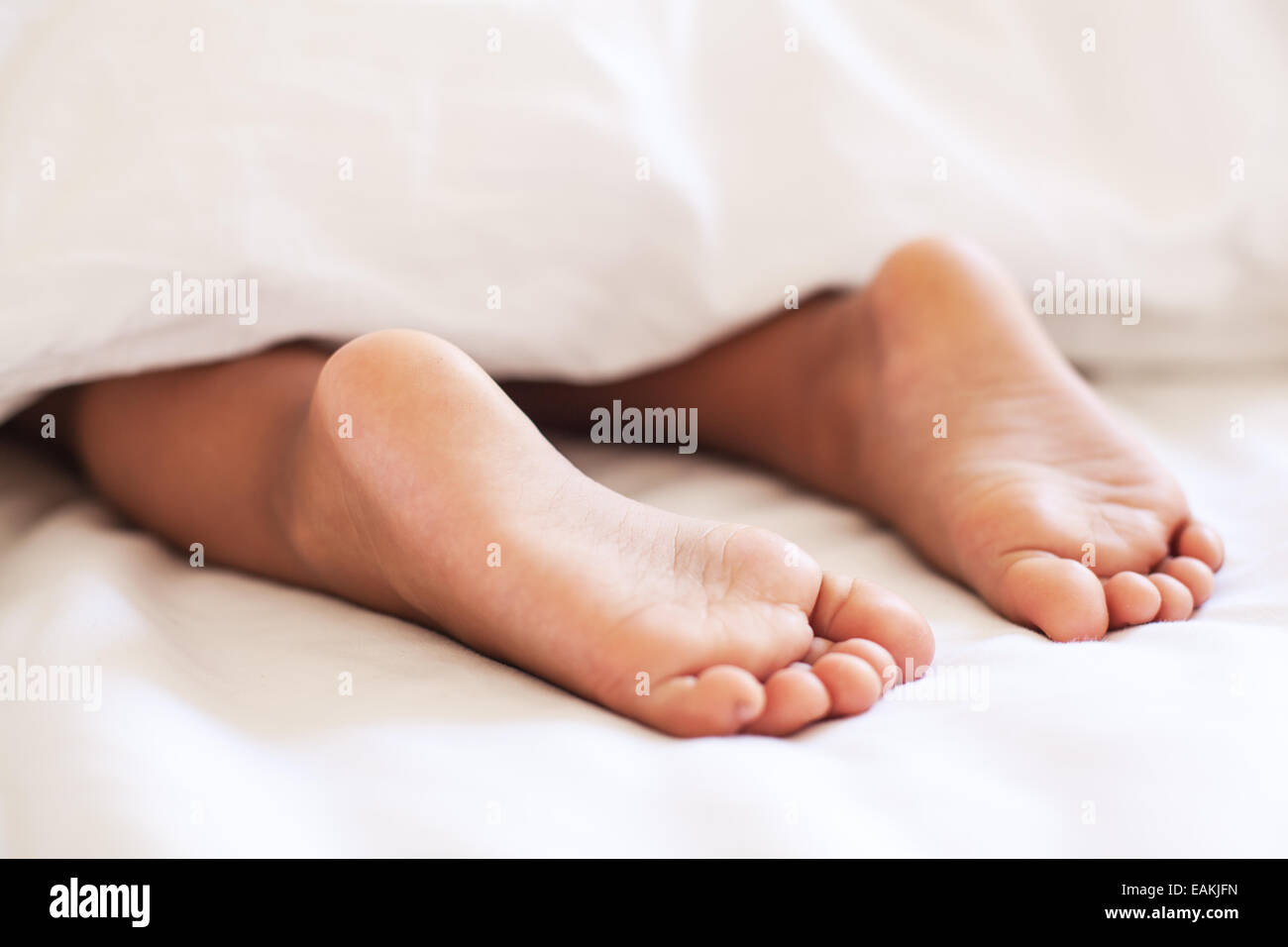 Füße des Kindes unter der weißen Decke. Stockfoto