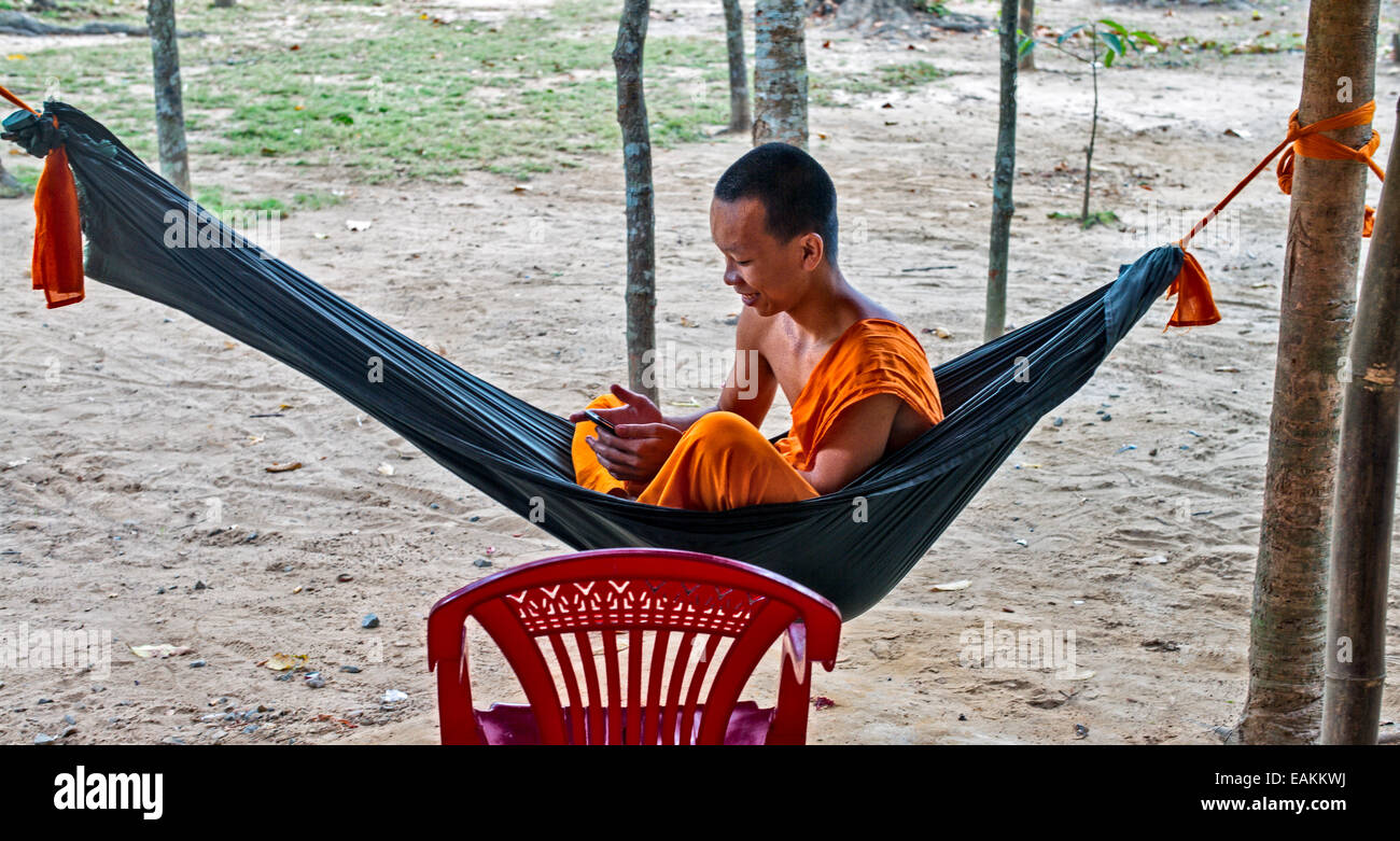 Junger vietnamesischer Mönch im Khmer-Theravada-buddhistischen Kloster in Tra Vinh entspannt in einer Hängematte mit seinem Handy. Stockfoto