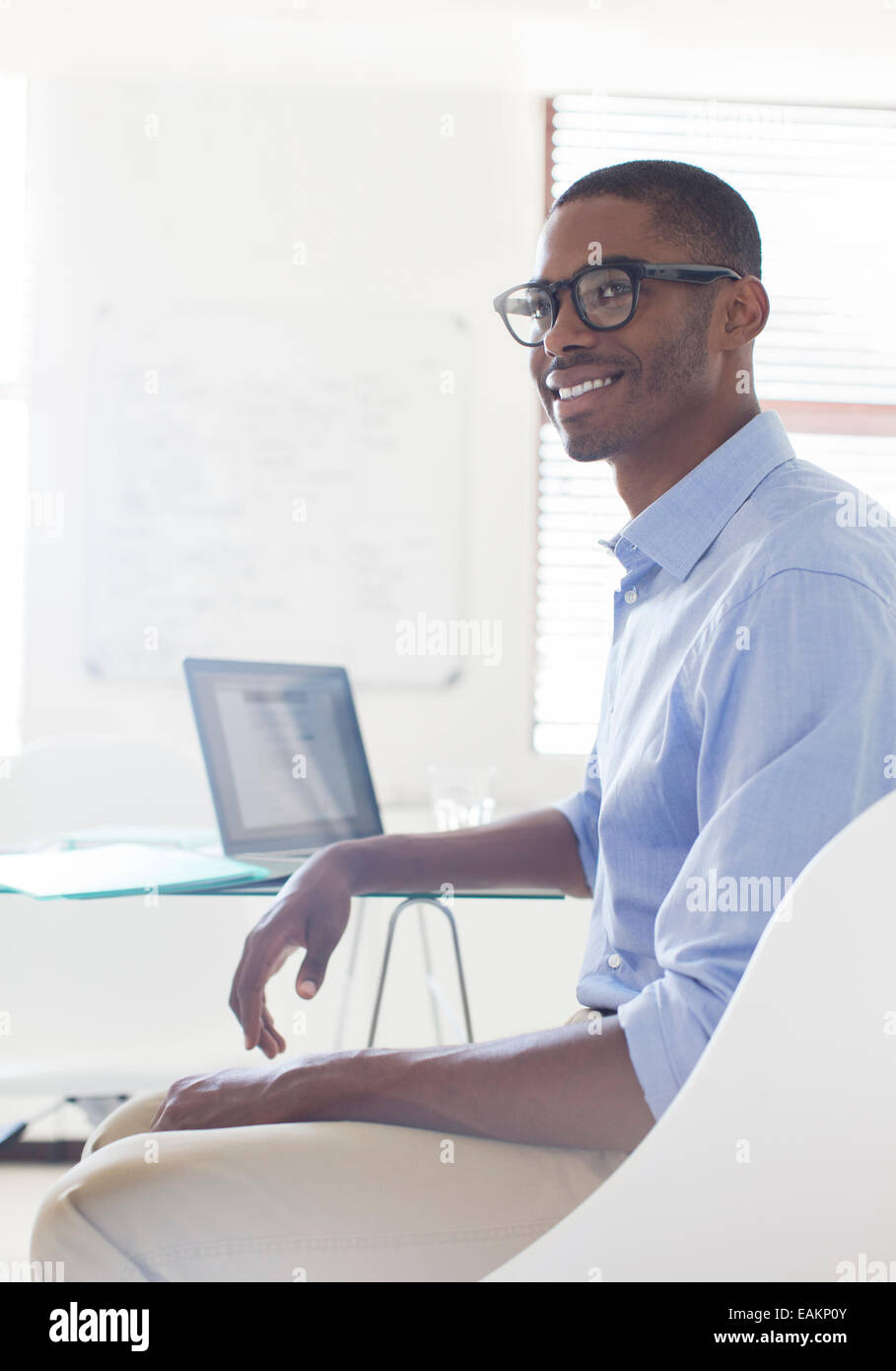 Porträt des jungen lächelnder Mann tragen Brillen und blaues Hemd sitzt am Schreibtisch mit laptop Stockfoto
