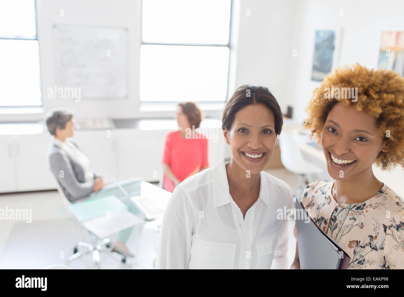 Porträt zweier lächelnd Geschäftsfrauen in Büro, Kollegen reden im Hintergrund Stockfoto