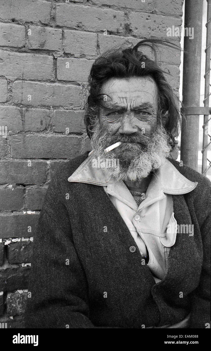 1970er Jahre, Porträt eines erwachsenen Mannes, mit wilden Haaren und ungepflegtem Bart und einer Zigarette im Mund, einer Person, die in harte Zeiten gefallen ist, obdachlos, ein Straßenmensch, Los Angeles, Kalifornien, USA. Teile von LA sind als „Pappstadt“ bekannt, wo eine große Anzahl verzweifelter Obdachloser auf der Straße leben. Stockfoto