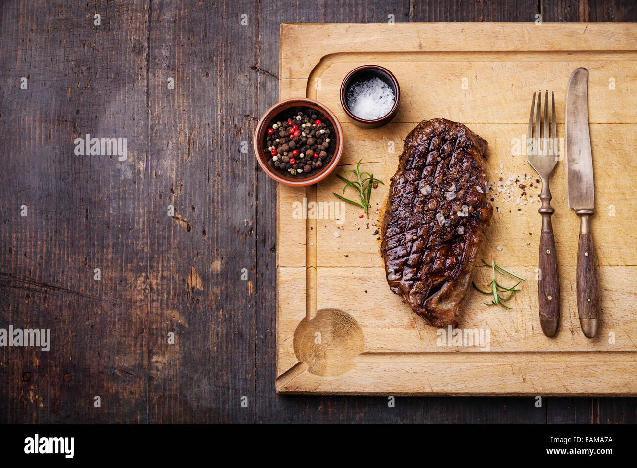 Gegrilltes New York Striploin Steak mit Salz und Pfeffer auf Fleisch Schneidbrett auf dunklem Holz Stockfoto