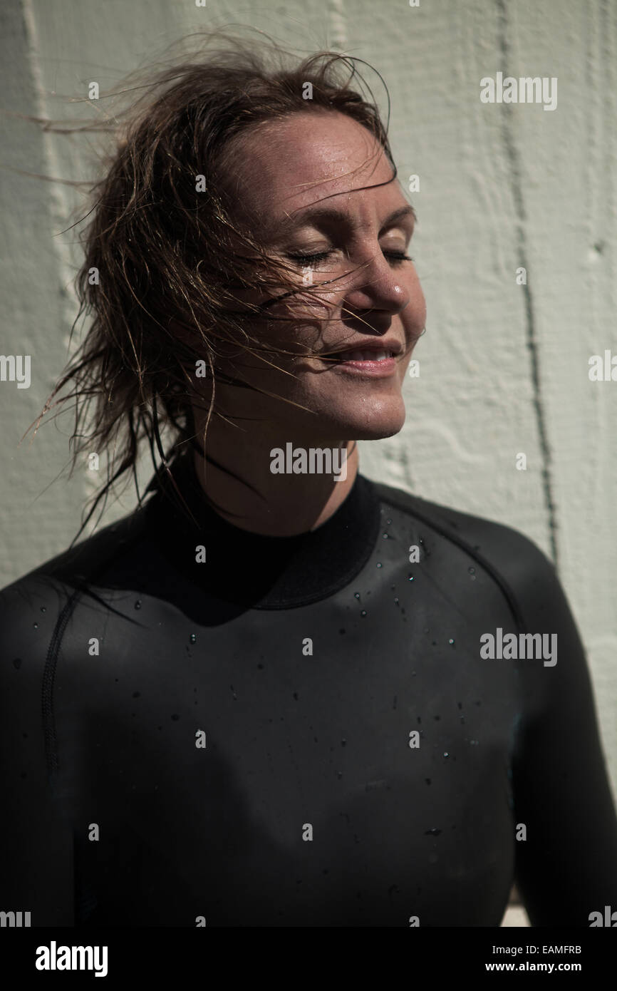 Attraktives Lächeln Brünette weibliche Schwimmer tragen schwarze Anzug mit nassen Haaren und geschlossenen Augen und Sonne im Gesicht Stockfoto