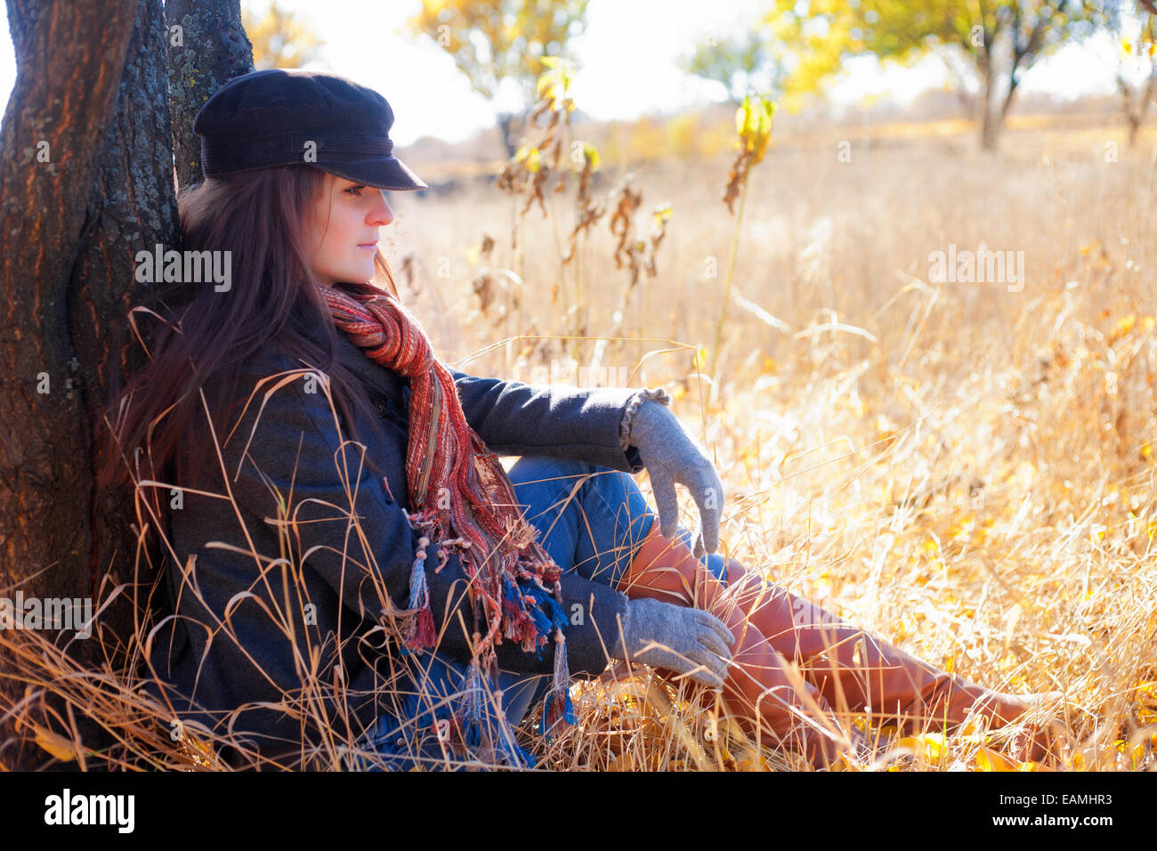 Mädchen sitzen in der Nähe eines Baumes im Herbst Stockfoto