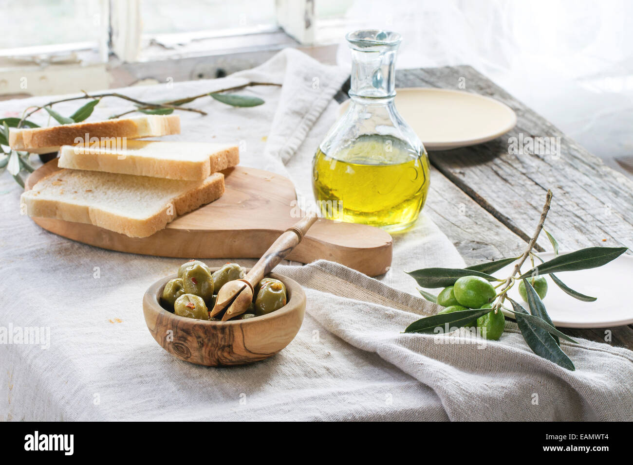 Mittagessen mit grünen Oliven, Brot und Olivenöl serviert auf alten Holztisch in der Nähe von Fenster. Stockfoto