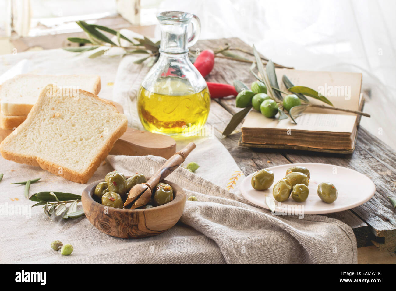 Mittagessen mit grünen Oliven, Brot und Olivenöl serviert mit Vintage Buches auf alten Holztisch in der Nähe von Fenster. Stockfoto