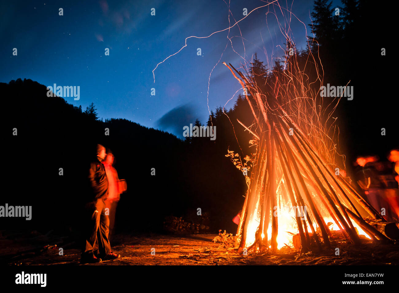 Zwei Menschen sitzen vor einem großen Lagerfeuer, durch die Nacht. Stockfoto