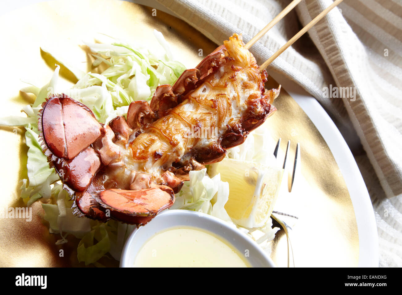 Main Hummerschwanz in der Shell-Blitz aufgespießt gebraten mit Zitronenbutter und Zitronen und Salat auf einem Teller gold Stockfoto