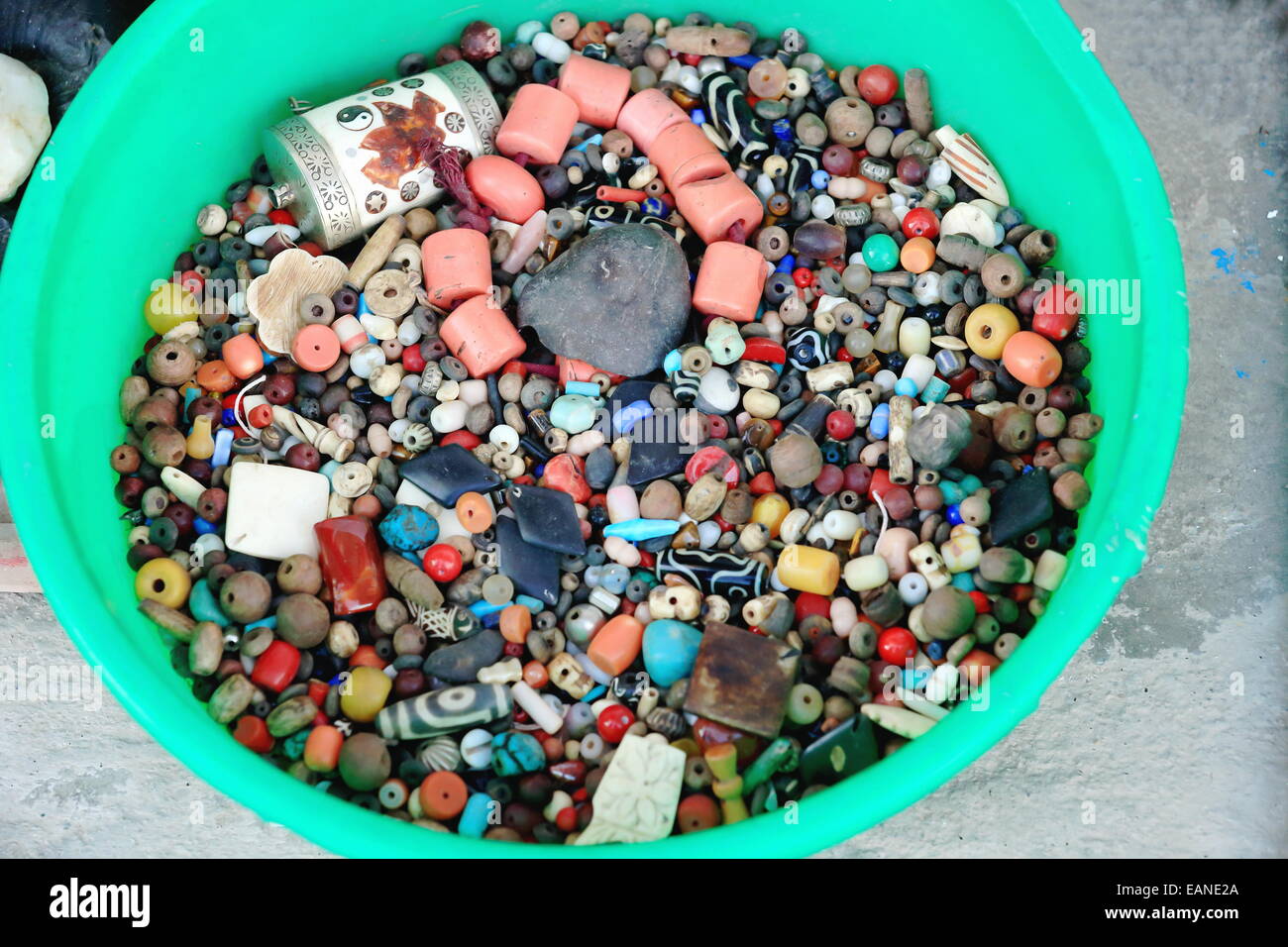 Viele bunte und vielgestaltige Steinperlen für die Collier-Set auf einem grünen Plastikeimer auf dem konkreten Bürgersteig vor einem Geschäft Stockfoto