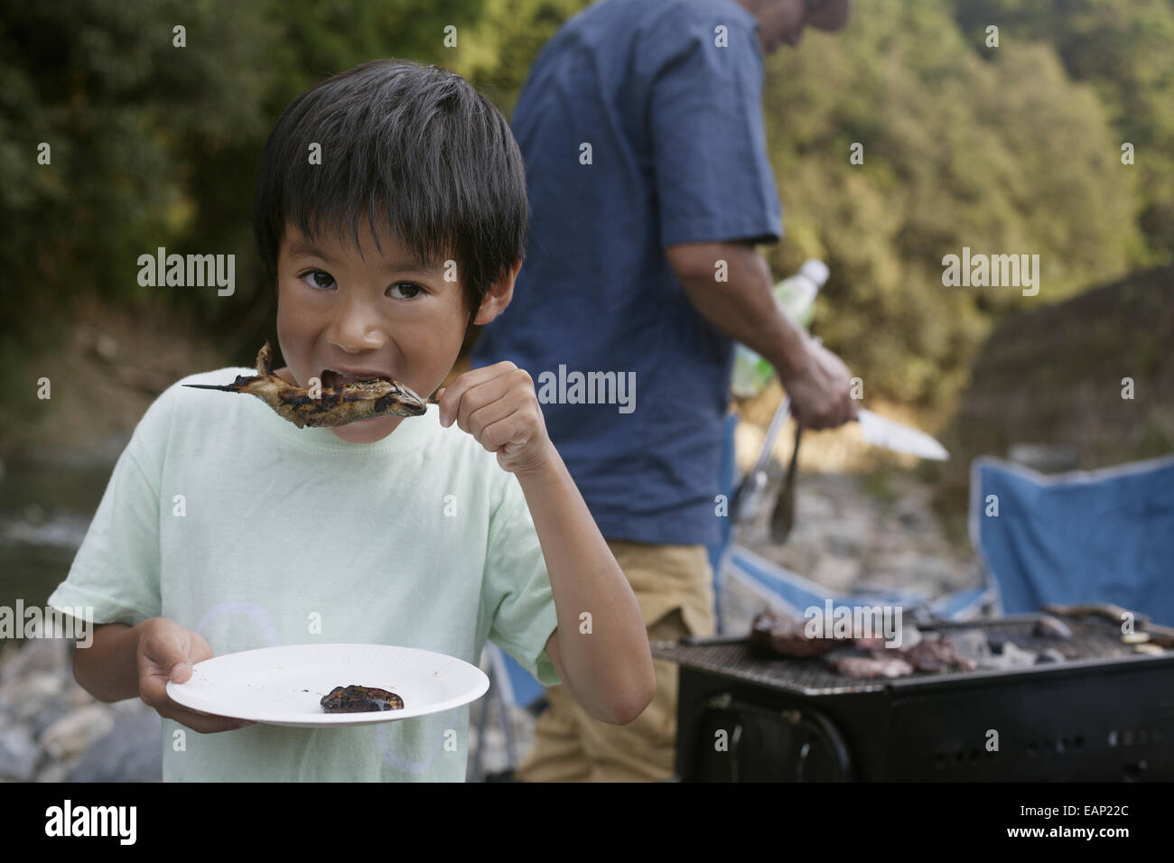 Kleiner Junge einen gegrillten Fisch zu essen, bei einem Picknick. Stockfoto