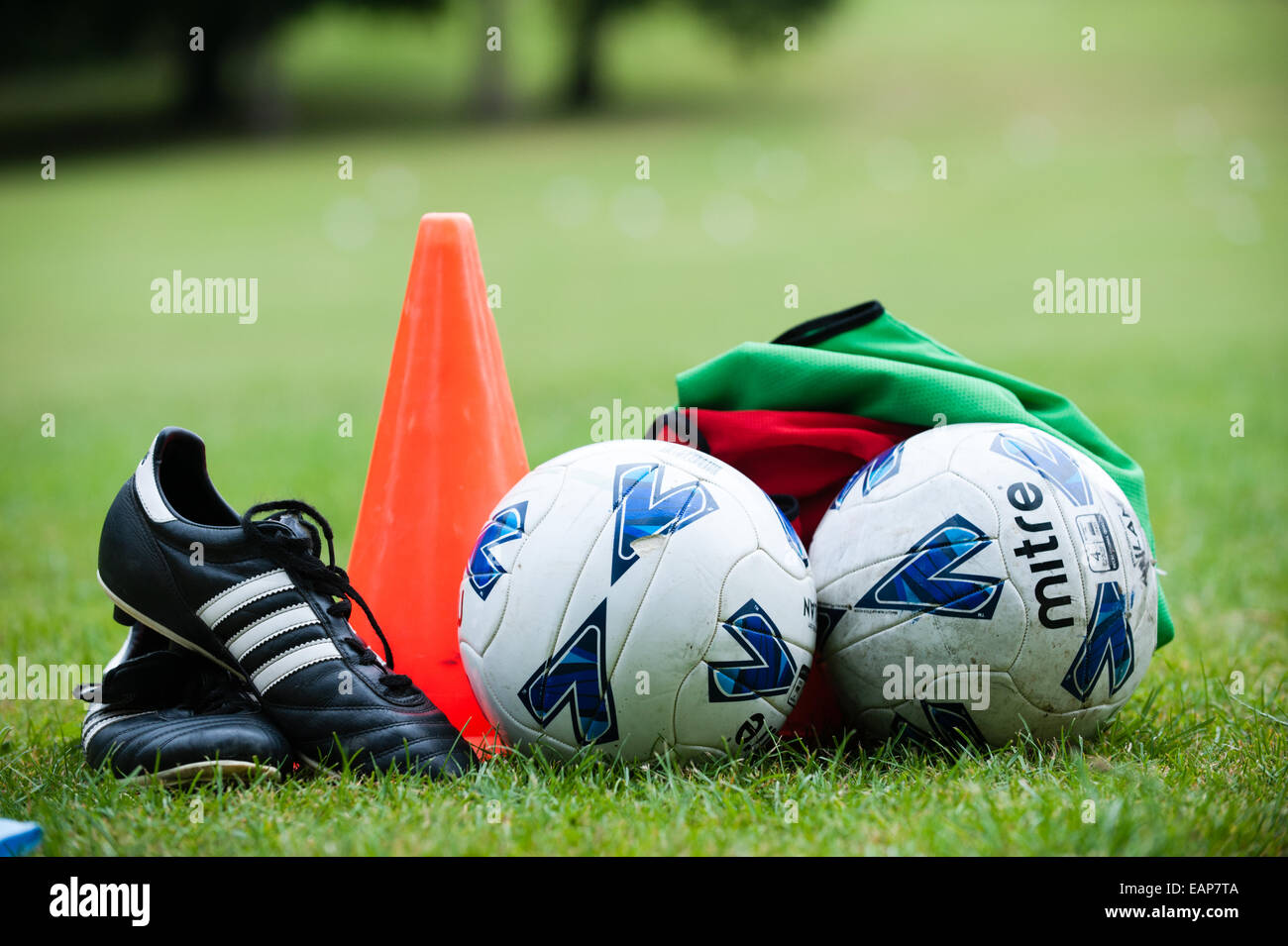 Fußballschuhe, einen roten Kegel, zwei Fußbälle und grünen und roten Tops auf dem Rasen wartet ein Ferien-Fußball-coaching-Kurs Stockfoto