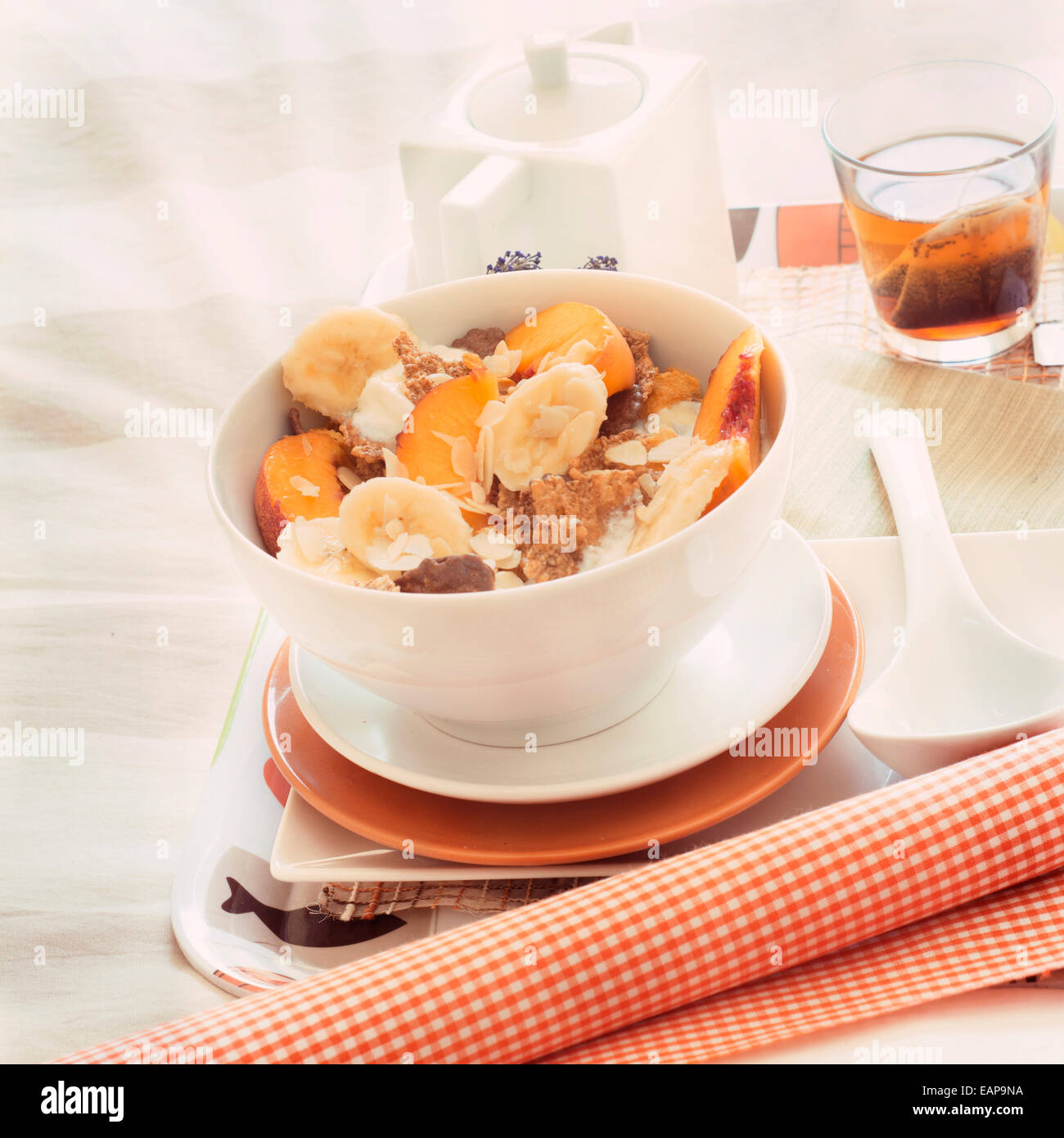Frühstück im Bett Tablett Müsli, Pfirsich und Banane, Joghurt und Tee, warme orange Farbe. Quadratisches Bild Stockfoto