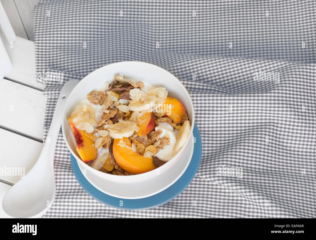 Frühstück im Bett Tablett Müsli, Pfirsich und Banane, Joghurt und Tee, warme blaue Farbe. Auf weißen Tischtuch und Holz Stockfoto