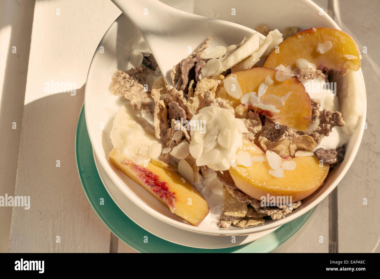 Frühstück in der Sonne, Müslischale, Pfirsich und Banane, Joghurt auf blaue Platte und warmen Vintage Farbe. Weiß auf Holz Stockfoto