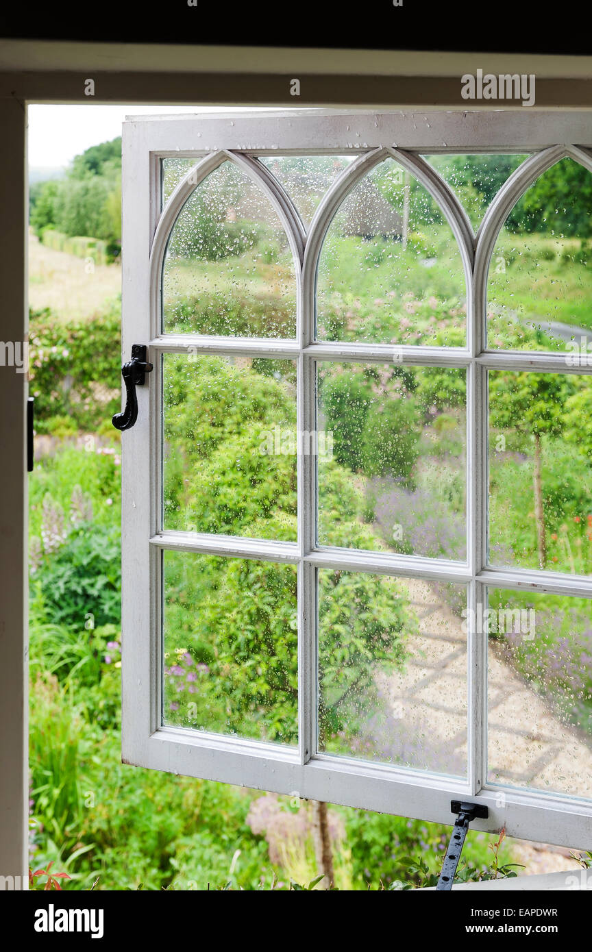 Blick durch offene gotische Fenster heraus auf üppig grünen Garten Stockfoto