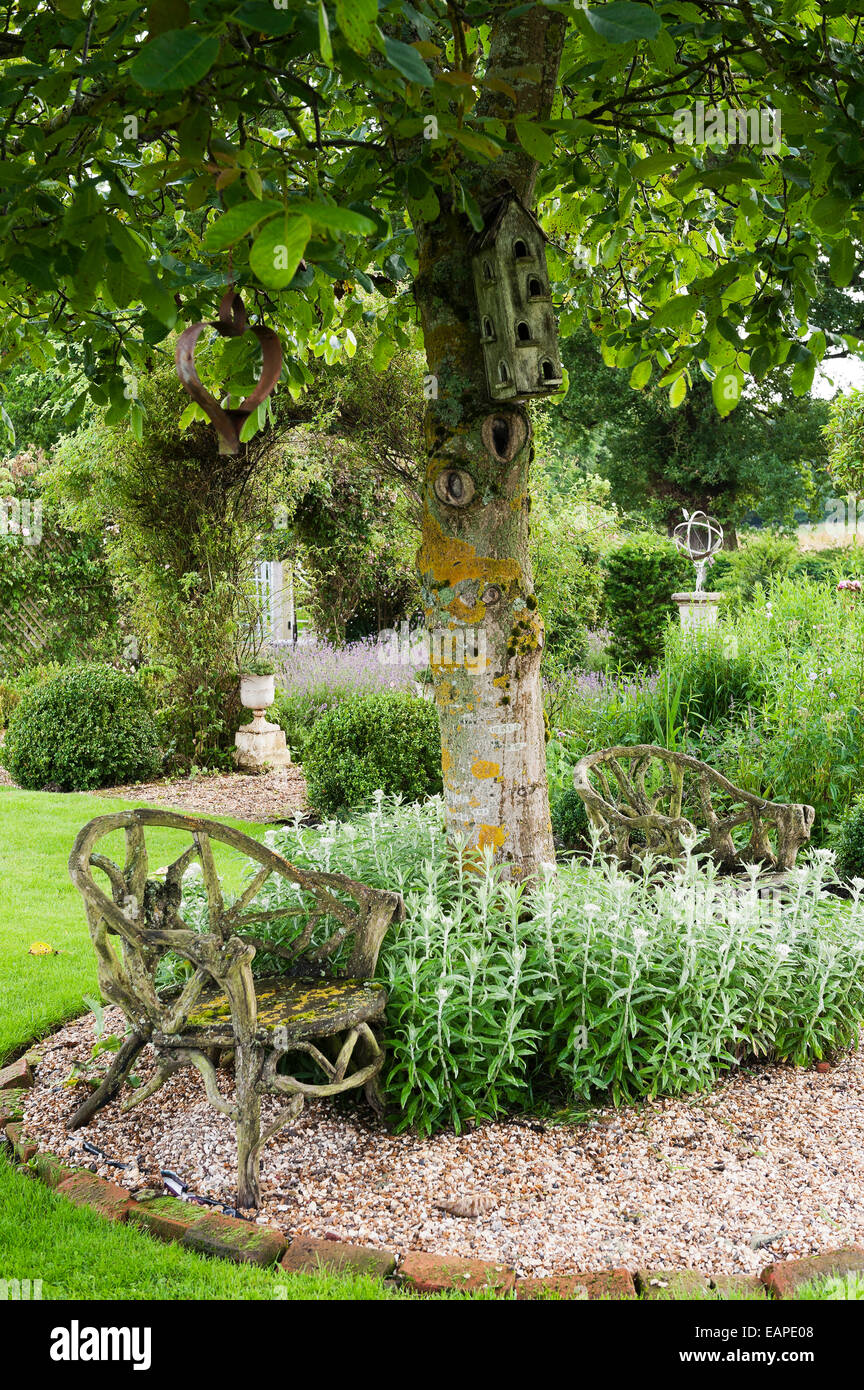 Alte hölzerne Stühle unter Baum in einem englischen Landhaus-Garten Stockfoto