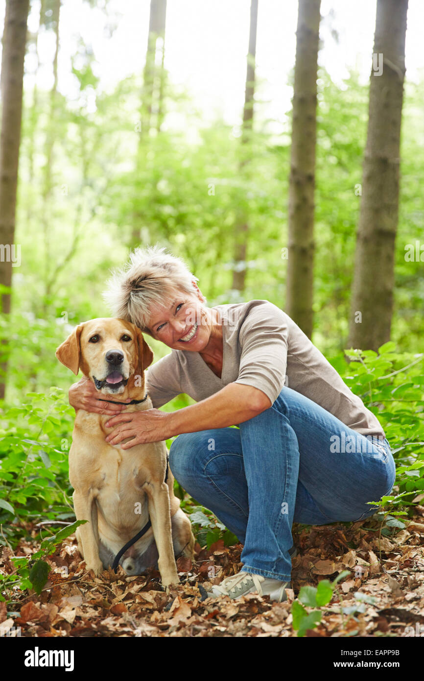 Ältere Frau mit Labrador Retriever Hund in einem Wald sitzt lächelnd Stockfoto
