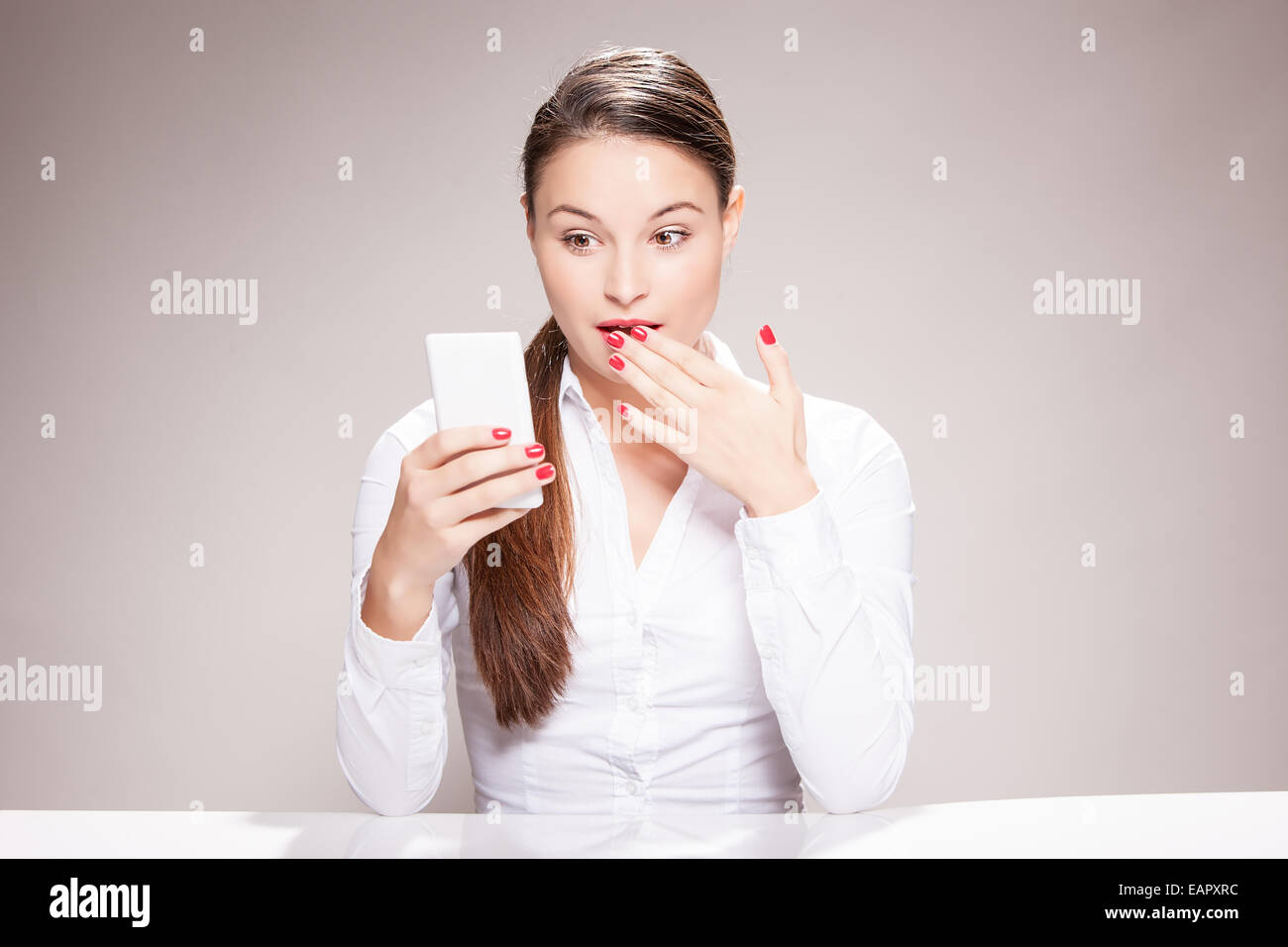 Attraktive junge Frau sitzend und mit Blick auf Smartphone. Stockfoto