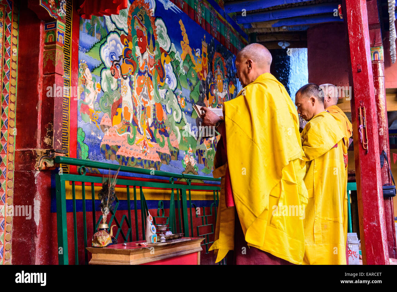 Drei Mönche von Lamayuru Gompa beten vor einer bunten religiösen Wandmalerei, Ladakh, Jammu und Kaschmir, Indien Stockfoto