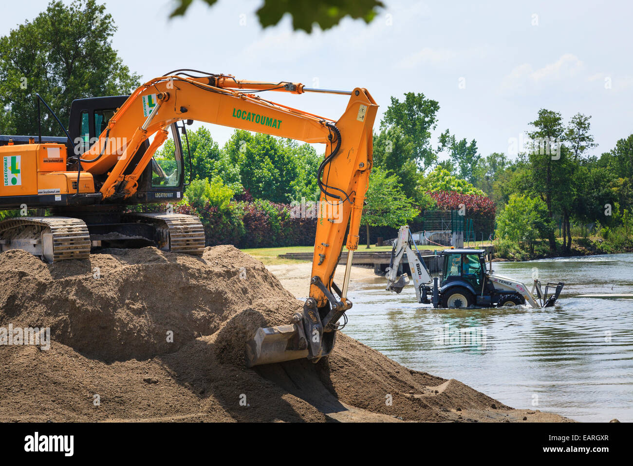 Verfolgten mechanischen Bagger sitzt auf einem Stapel des Bodens mit einem Traktor Bagger mit Tieflöffel in den Fluss Baggerarbeiten Stockfoto