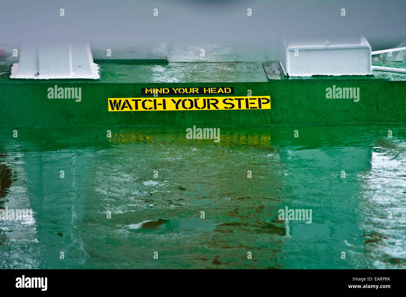 Ein Schild warnt vor eine niedrige Decke und versteckte Schritt auf einem nassen Schiffsdeck. Stockfoto