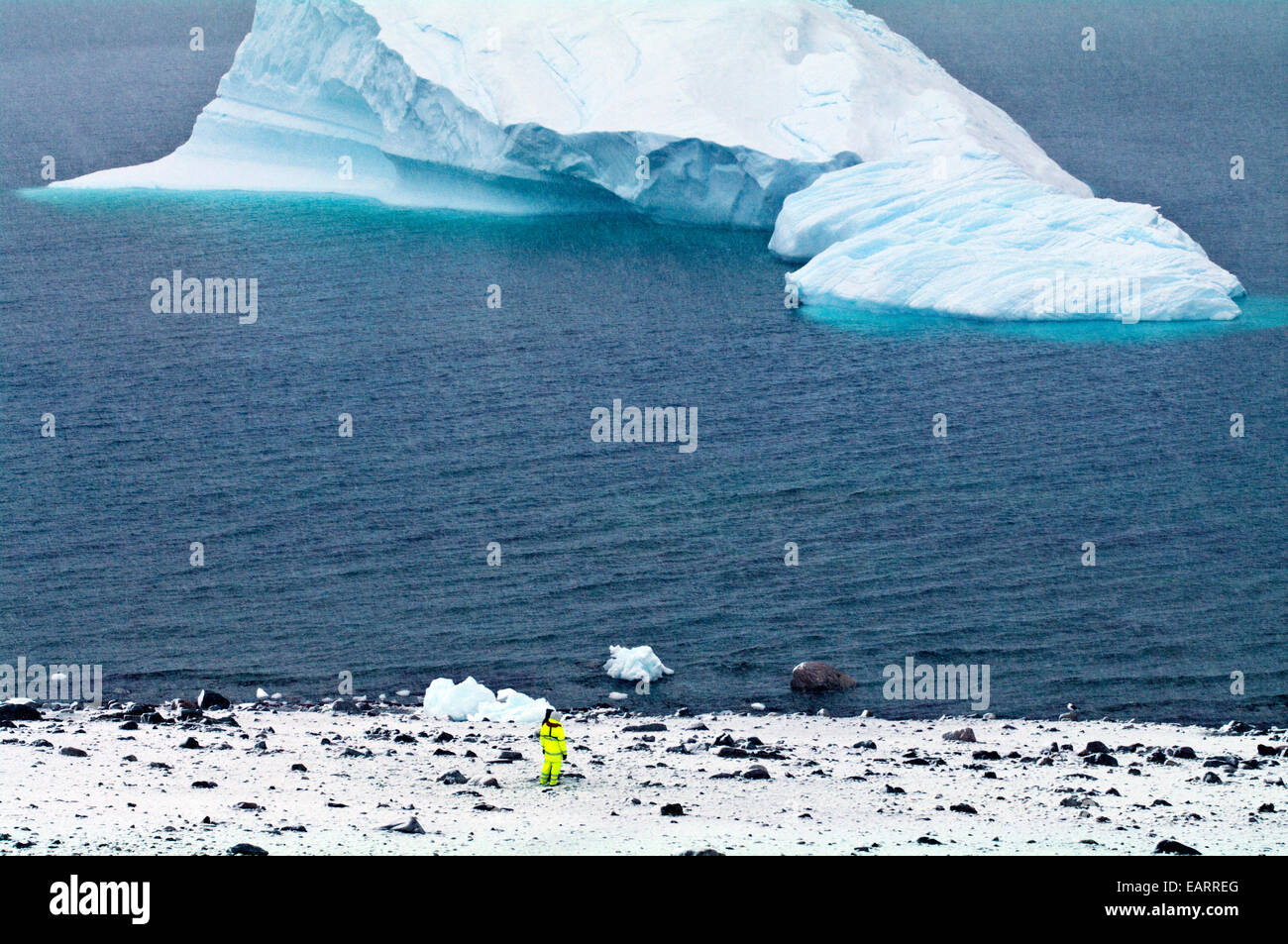 Ein Tourist in fluoreszierende Kleidung Uhren einen Eisberg in der Nähe der Küste. Stockfoto