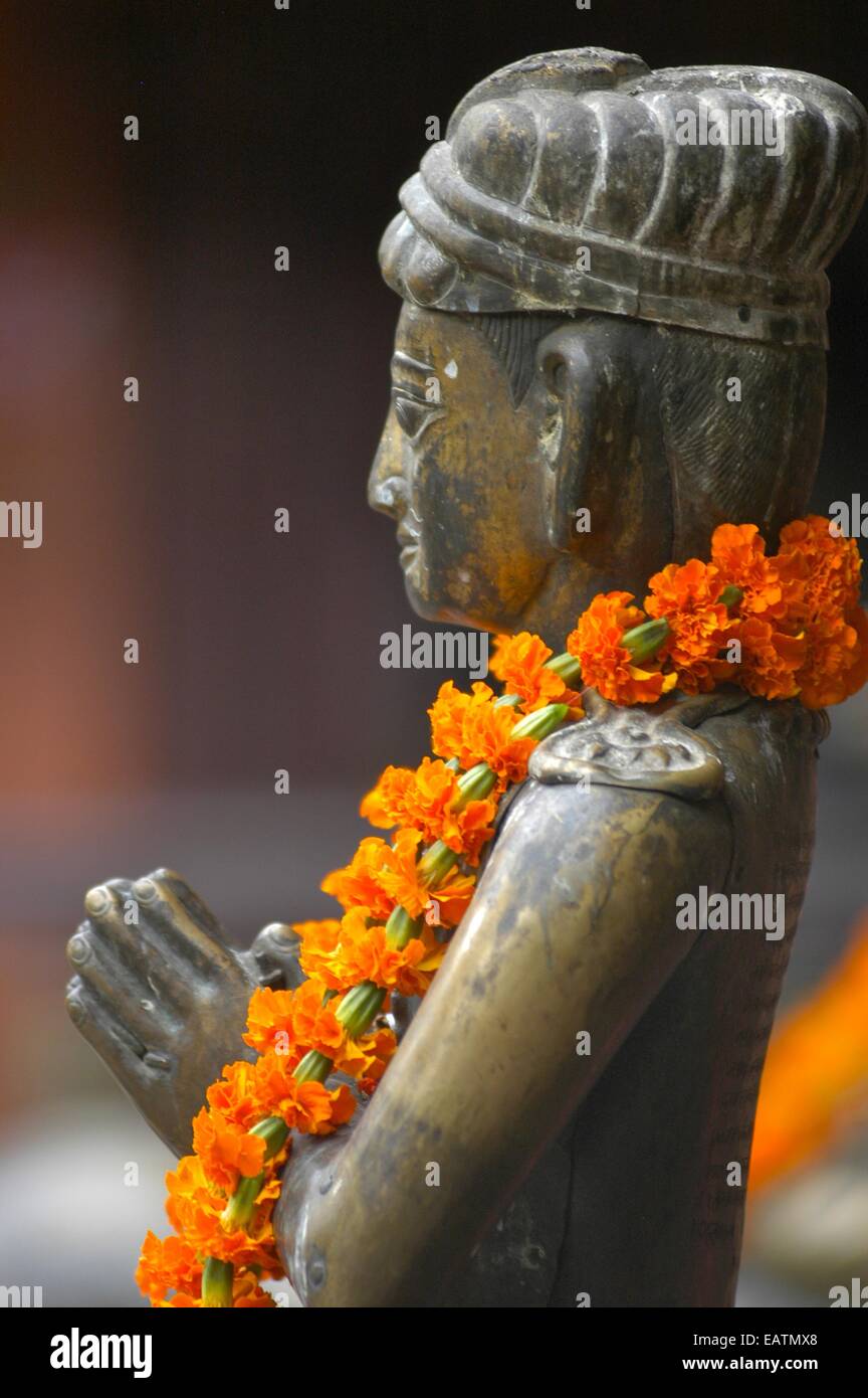 Eine Girlande aus Ringelblumen drapiert über eine Statue von Buddha zu beten. Stockfoto