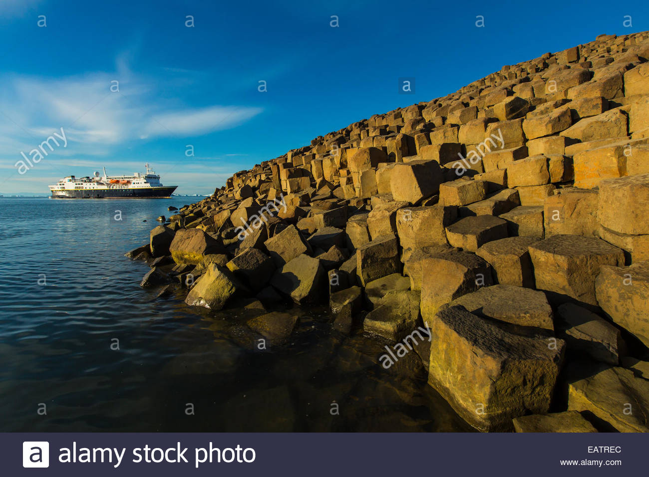 Ein Kreuzfahrtschiff in der Ferne über säulenförmigen gegliederte Basalt. Stockfoto