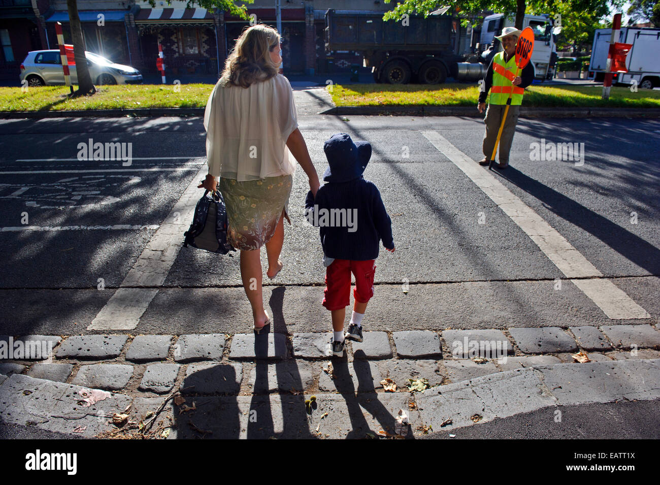 Eine Mutter überquert eine stark befahrene Straße mit ihrem Sohn auf seinen ersten Schultag. Stockfoto