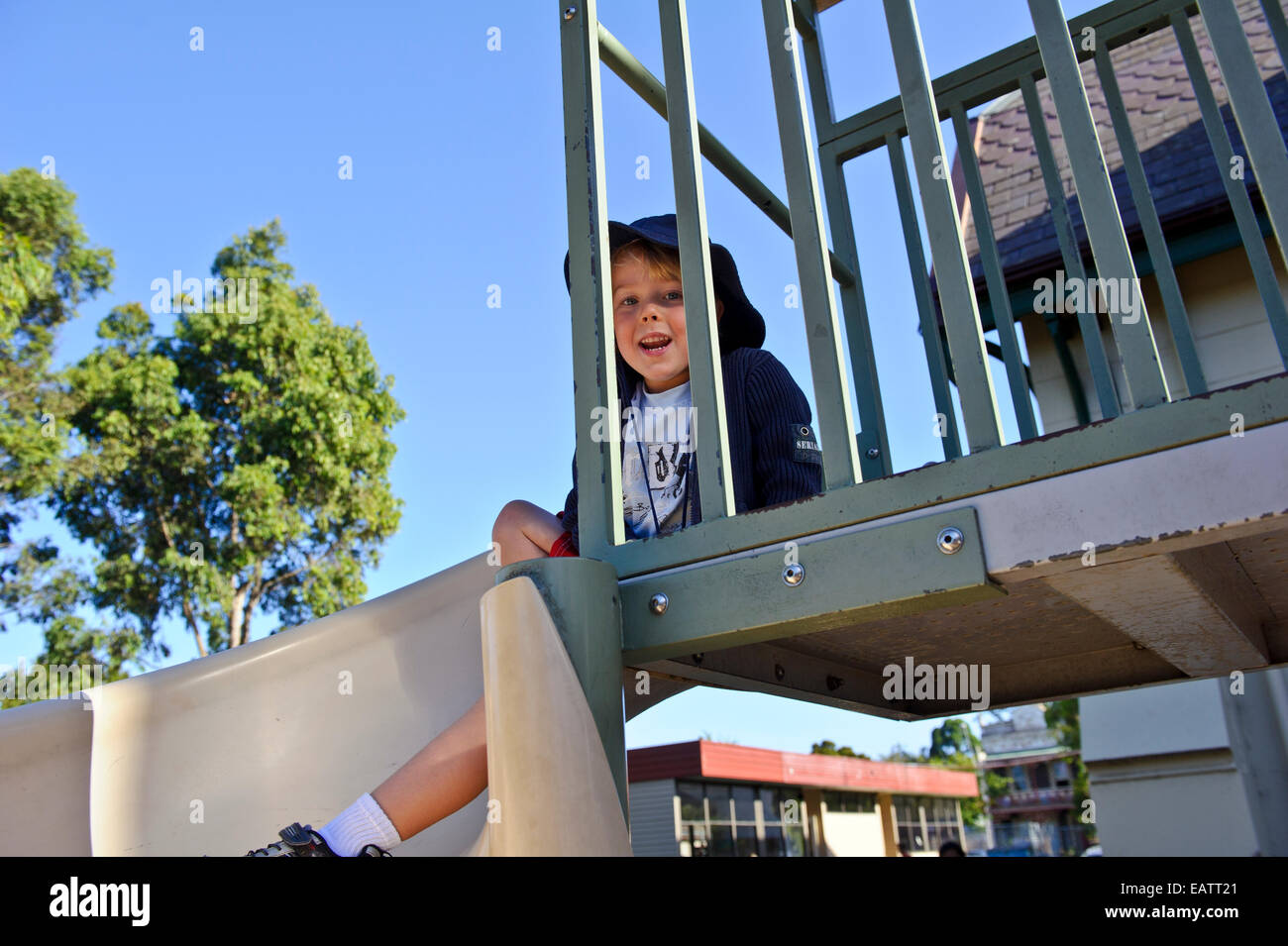 Ein Junge spielt auf einer Rutsche auf dem Spielplatz an seinem ersten Tag der Schule. Stockfoto