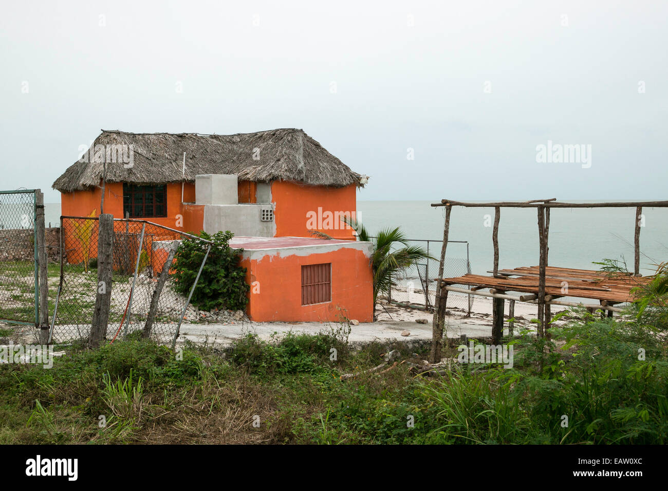 Mexikanisches Haus am Wasser mit traditionellem Strohdach und orangefarbenen Stuckwänden. Stockfoto