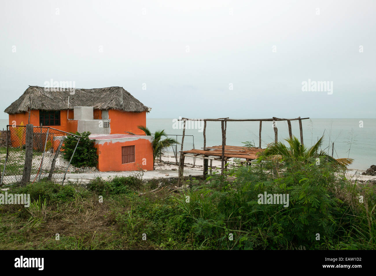 Mexikanisches Haus am Wasser mit traditionellem Strohdach und orangefarbenen Stuckwänden. Stockfoto