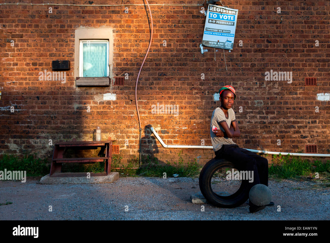 Ein Teenager Junge sitzt auf einem Reifen und springt einen Fußball auf seine Füße in einem der Durban Deep alten Hostels am Stadtrand von Stockfoto