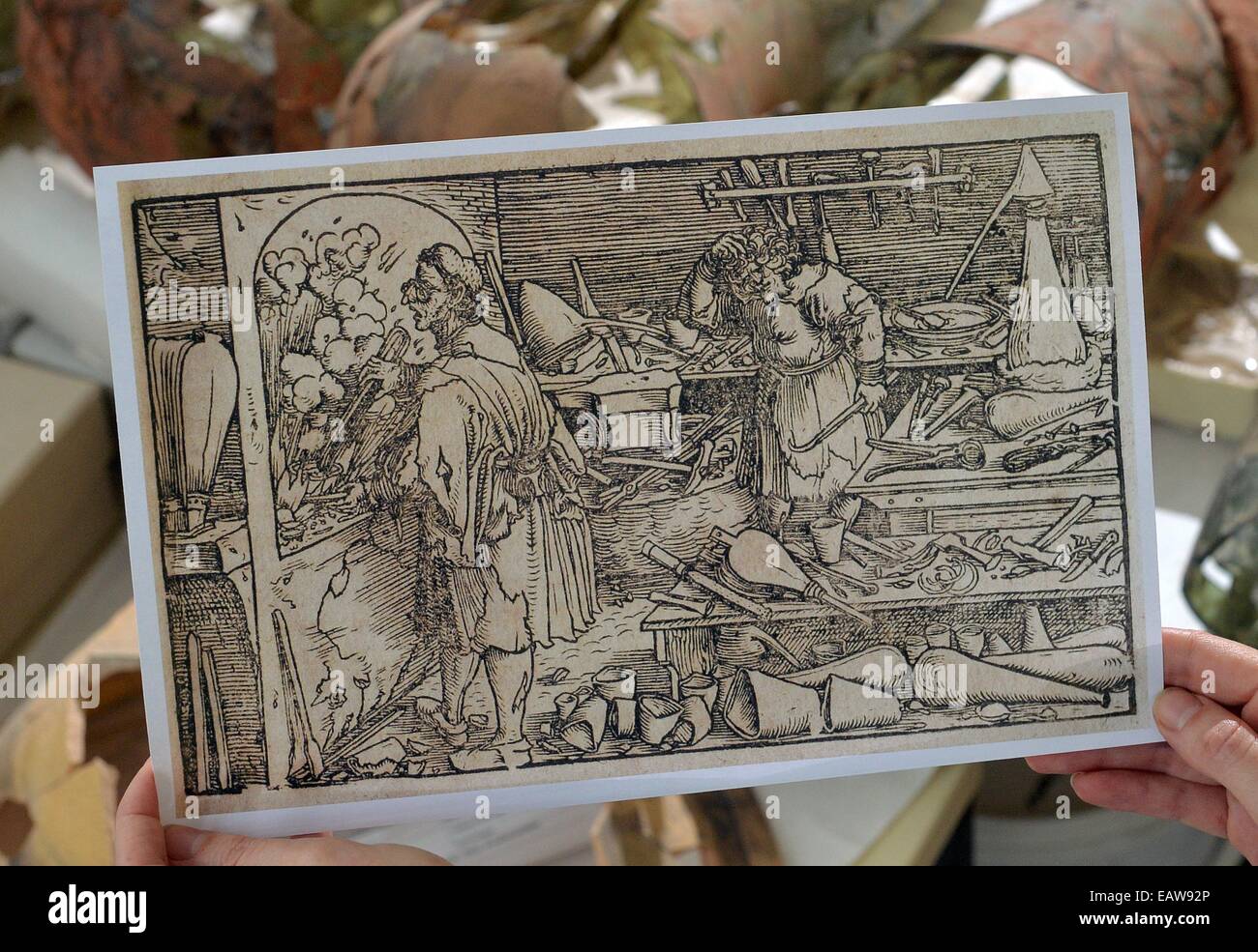 Die Kopie eines Druckes mit der Szene von einem Alchemisten Workshop findet mein Angestellter aus dem Landesmuseum für Vorgeschichte hält ein Stück von einem Becherglas aus dem rund 500 Jahre alten Alchemie-Workshop in Halle, Deutschland, 18. November 2014. Die Stücke ausgegraben in 2012 und jetzt restauriert sind die ältesten erhaltenen ihrer Art in Mitteleuropa. Wissenschaftler sprechen von einer einzigartigen und außergewöhnlichen Entdeckung. Es bleibt Spekulation, wenn das Objekt aus der historischen Figur Dr. Johann Georg Faustus, der Reisen Wunderheiler war, lebte eine Zeitlang in Wittenberg. Foto: HENDRIK SCHMID Stockfoto