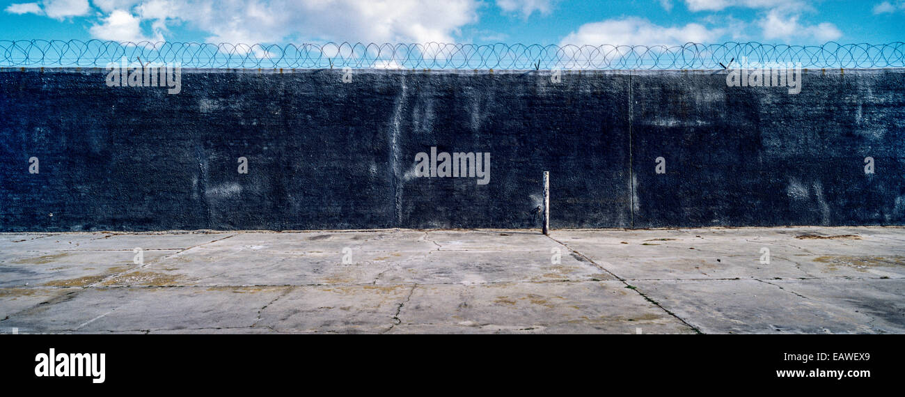 Eine karge strukturlose konkrete Gefängnis Hof Mauer mit Stacheldraht gekrönt. Stockfoto