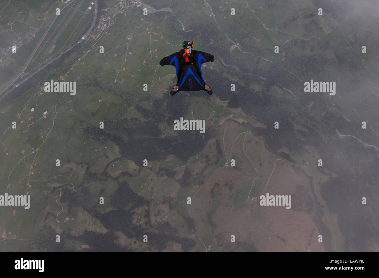 Die Fallschirmspringer fliegt in einem Wingsuit über grüne Felder in Richtung Meer & er abtauchen und den Anzug testen. Stockfoto