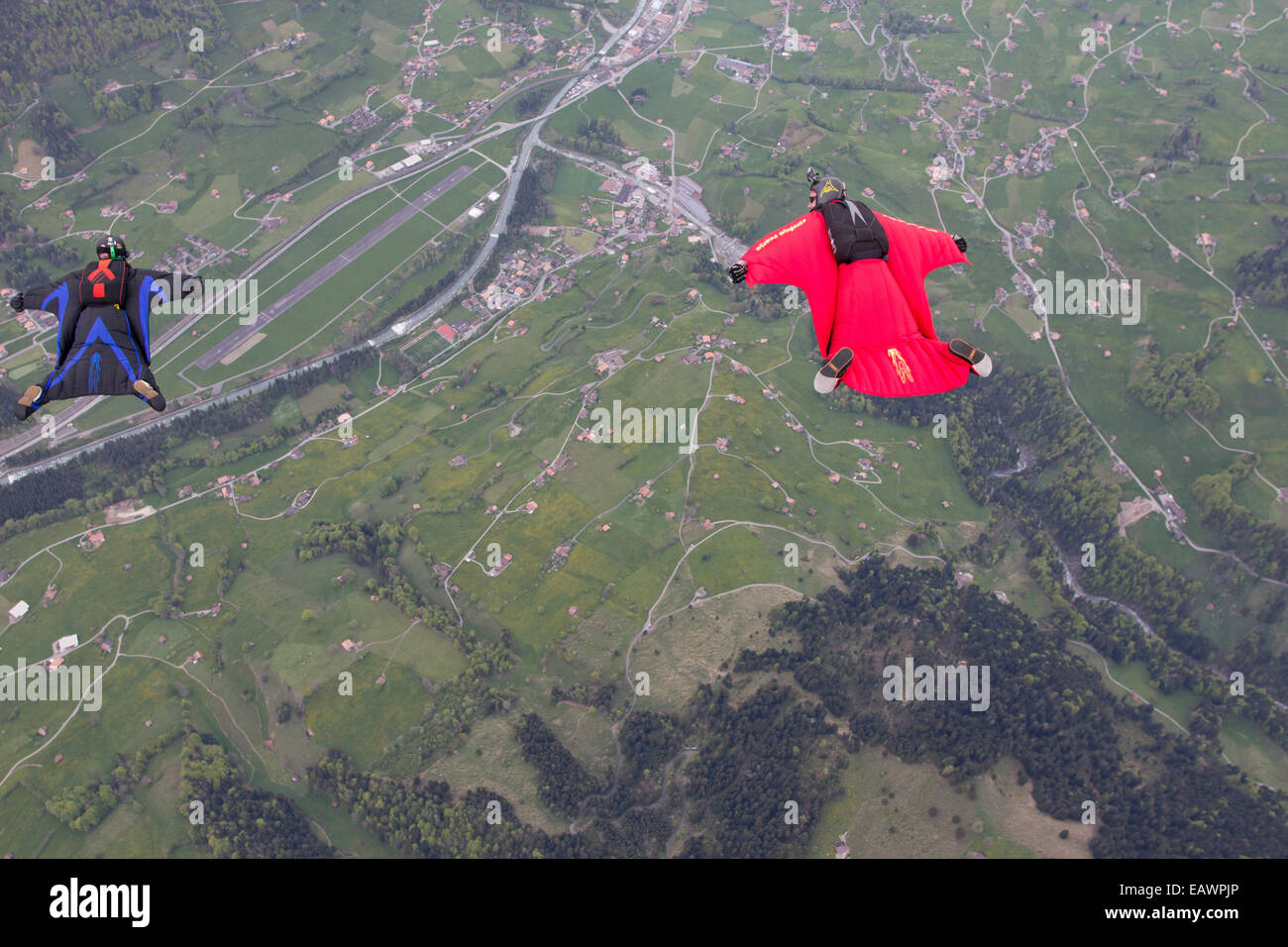 Diese Fallschirmspringer fliegt in einem Wingsuit über grüne Felder in Richtung Meer & sie abtauchen und den Anzug testen. Stockfoto