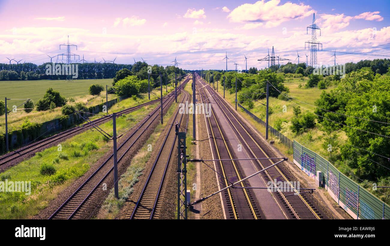 Schienen in Landschaft, grüne Wiesen, blauer Himmel violett Stockfoto