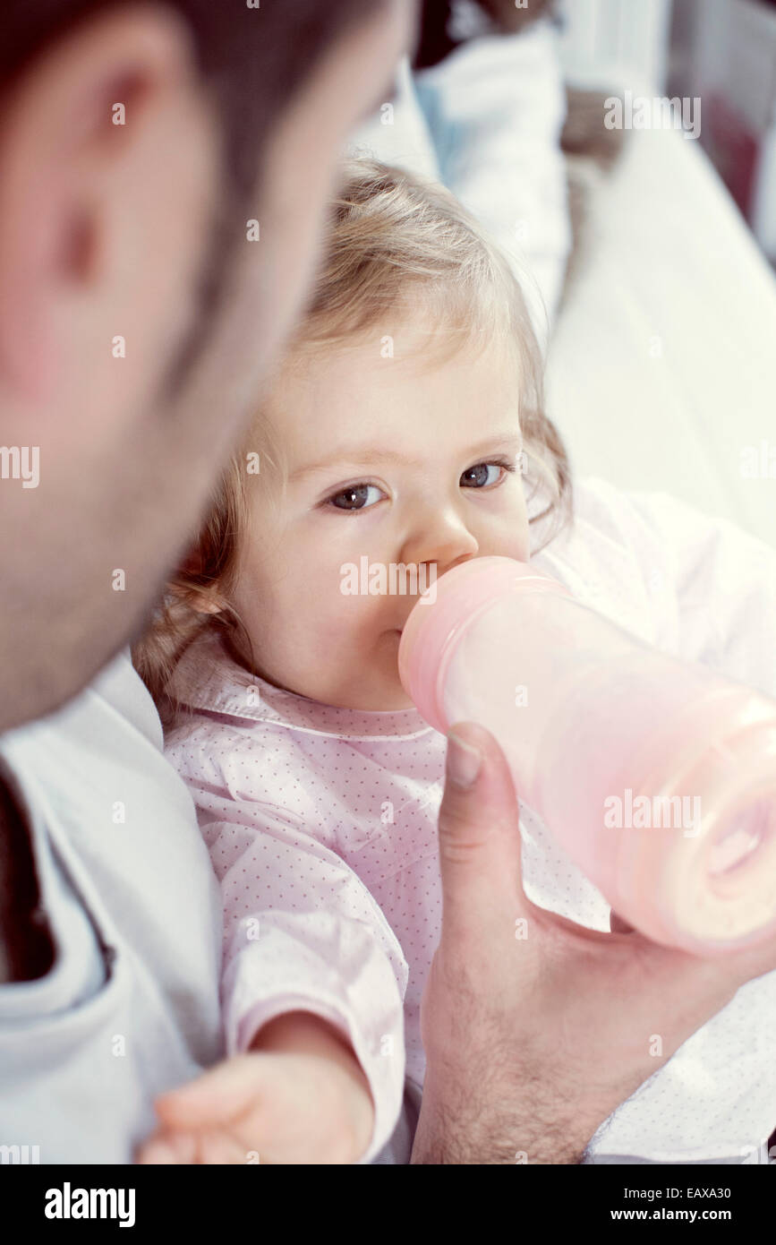 Babymädchen trinken aus der Flasche mit der Hilfe des Vaters Stockfoto