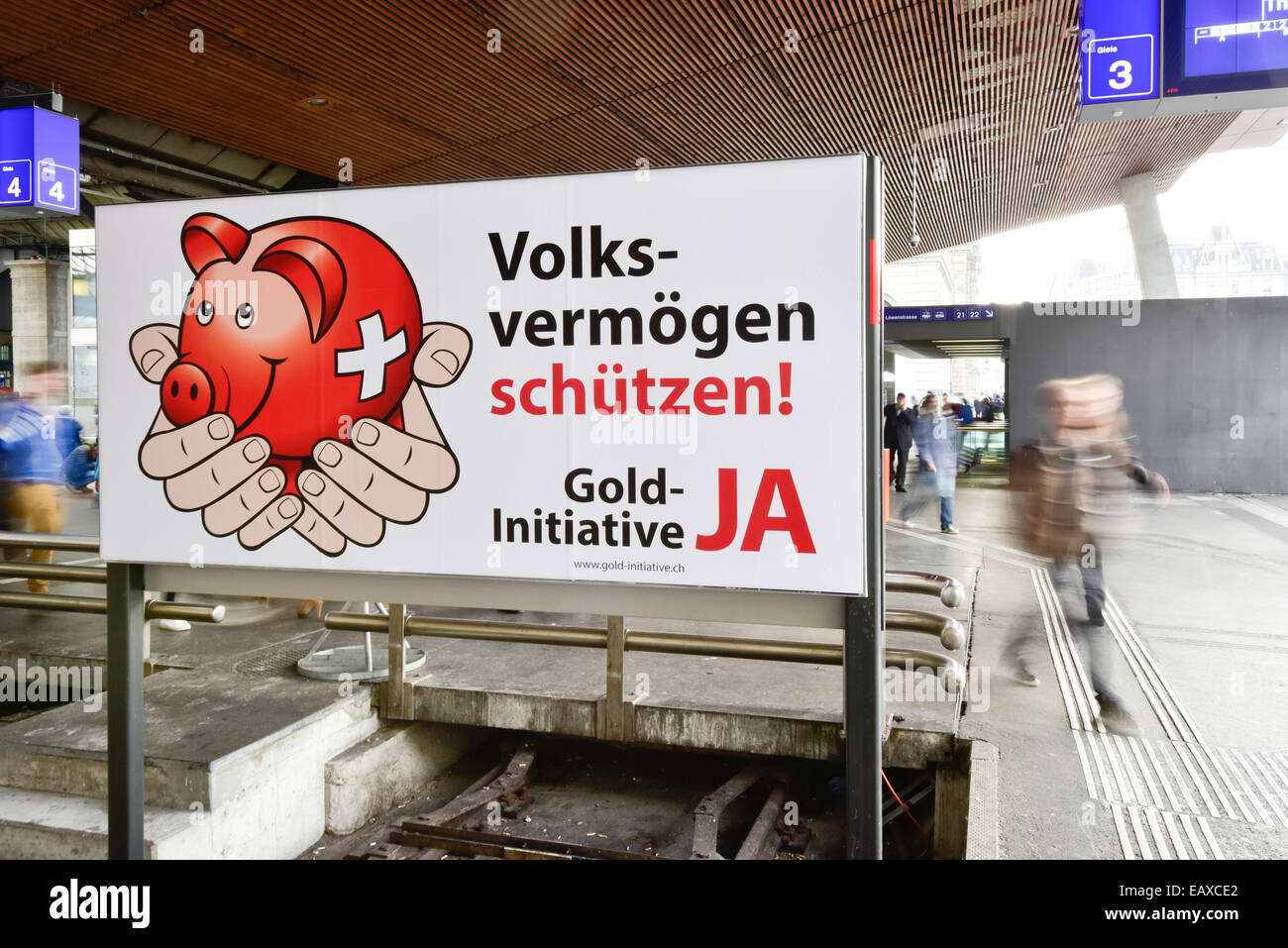 Zürich, Schweiz. 21. November 2014. Menschen im Zürcher Hauptbahnhof sind hinter einem Referendum Wahlplakat der Schweizer "Gold-Initiative" Volksabstimmung übergeben, die am 30. November 2014 stattfinden soll. Mit einer Woche zu gehen wird die Kampagne für das Referendum der Schweizer Gold-Initiative in voller Stärke in der ganzen Schweiz. Das umstrittene Referendum strebt zu zwingen, die Schweizerische Nationalbank, mindestens 20 % aller Vermögenswerte in physisches Gold zu halten. Bildnachweis: Erik Tham/Alamy Live-Nachrichten Stockfoto