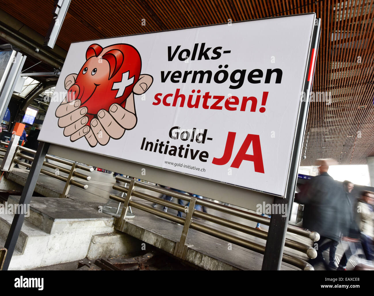 Zürich, Schweiz. 21. November 2014. Menschen im Zürcher Hauptbahnhof sind hinter einem Referendum Wahlplakat der Schweizer "Gold-Initiative" Volksabstimmung übergeben, die am 30. November 2014 stattfinden soll. Mit einer Woche zu gehen wird die Kampagne für das Referendum der Schweizer Gold-Initiative in voller Stärke in der ganzen Schweiz. Das umstrittene Referendum strebt zu zwingen, die Schweizerische Nationalbank, mindestens 20 % aller Vermögenswerte in physisches Gold zu halten. Bildnachweis: Erik Tham/Alamy Live-Nachrichten Stockfoto